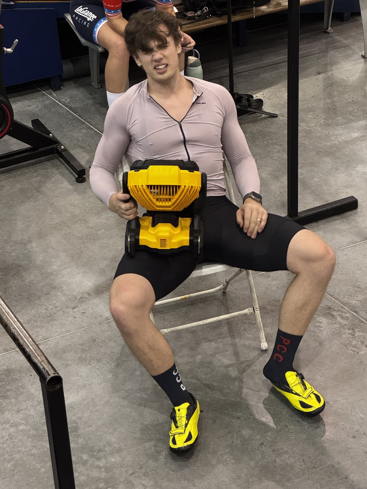 Matthew in race kit, sitting at the velodrome with a portable fan, recovering between efforts